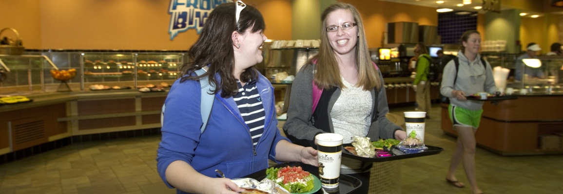 Students walking with food trays in the dining hall.