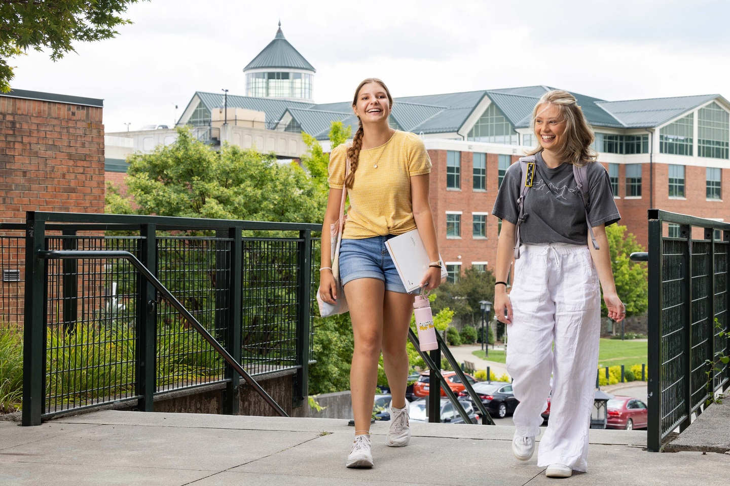 Two female students touring campus with Library in the backgound